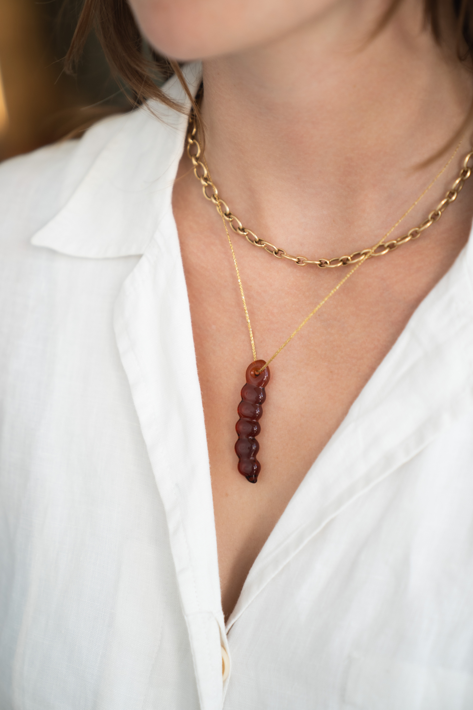 A close-up of a model wearing a layered necklace set. The set features a gold chain with a vertical strand of faceted dark amber beads pendant.