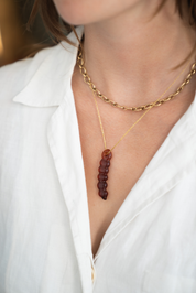 A close-up of a model wearing a layered necklace set. The set features a gold chain with a vertical strand of faceted dark amber beads pendant.