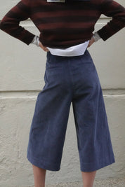 Woman wearing long blue corduroy shorts, with a brown striped cashmere jumper and navy scarf. 