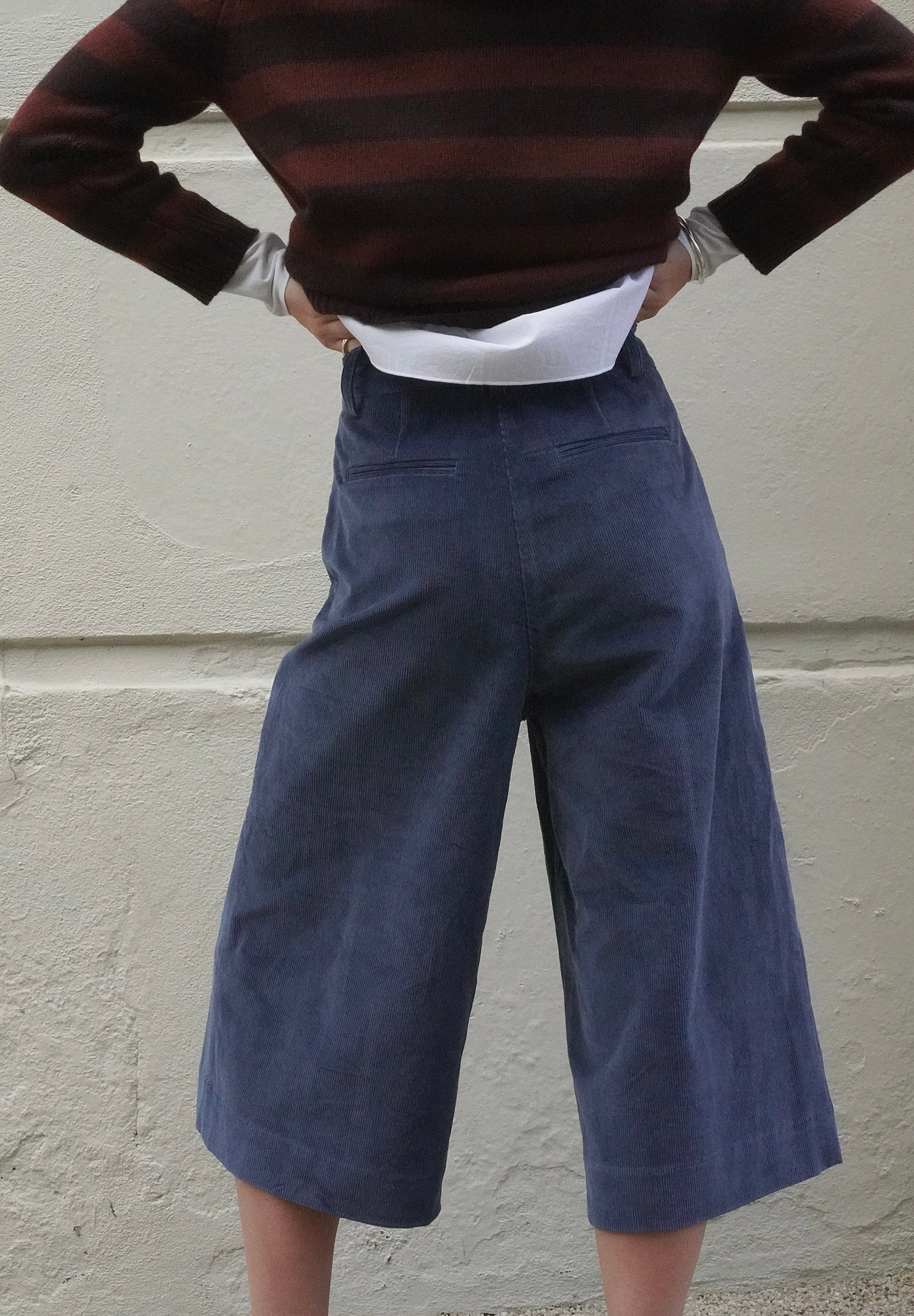 Woman wearing long blue corduroy shorts, with a brown striped cashmere jumper and navy scarf. 