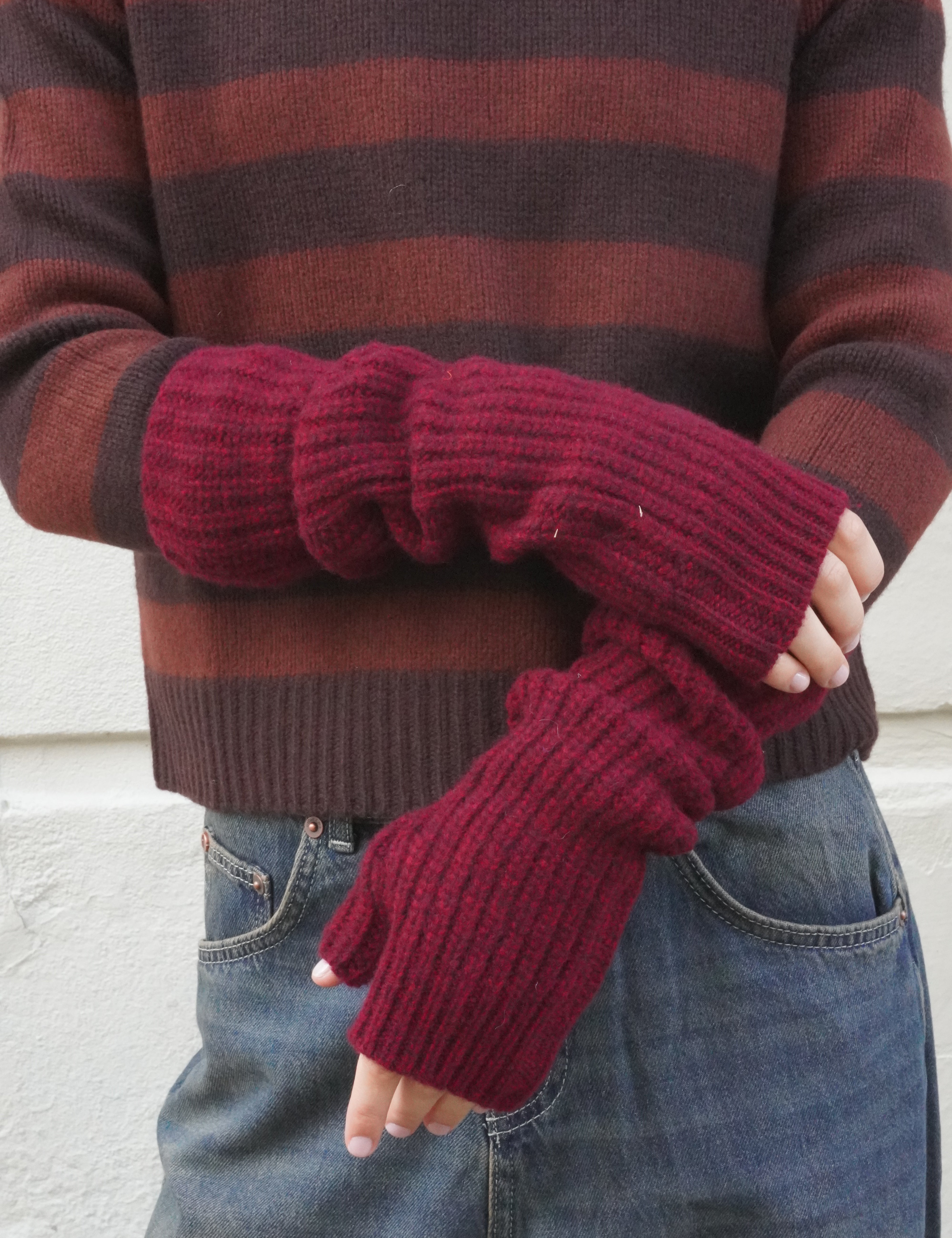 Woman wearing red berry wool open rib fingerless gloves, and a brown striped cashmere jumper. 