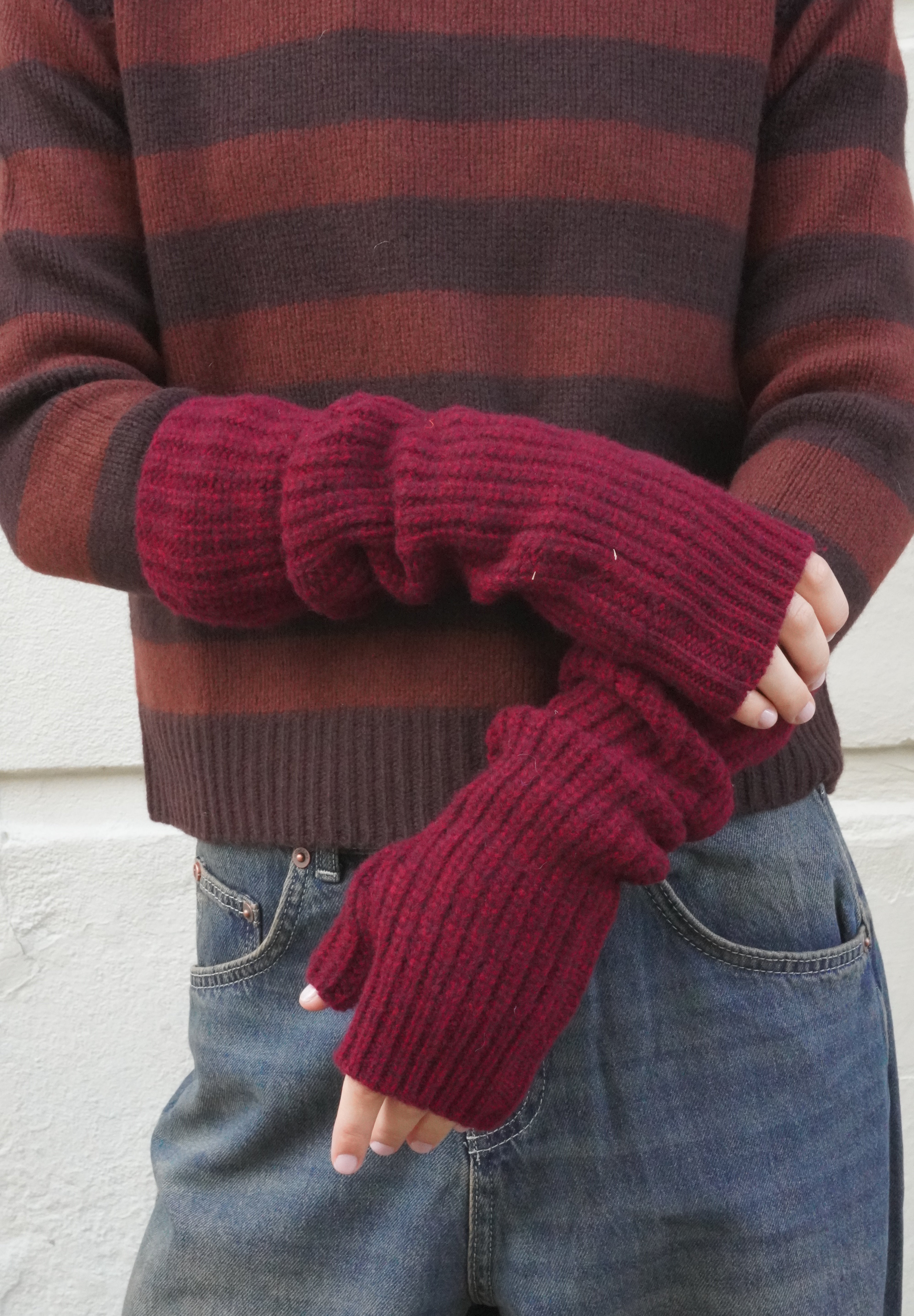 Woman wearing red berry wool open rib fingerless gloves, and a brown striped cashmere jumper. 