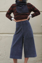 Woman wearing long blue corduroy shorts, with a brown striped cashmere jumper and navy scarf. 