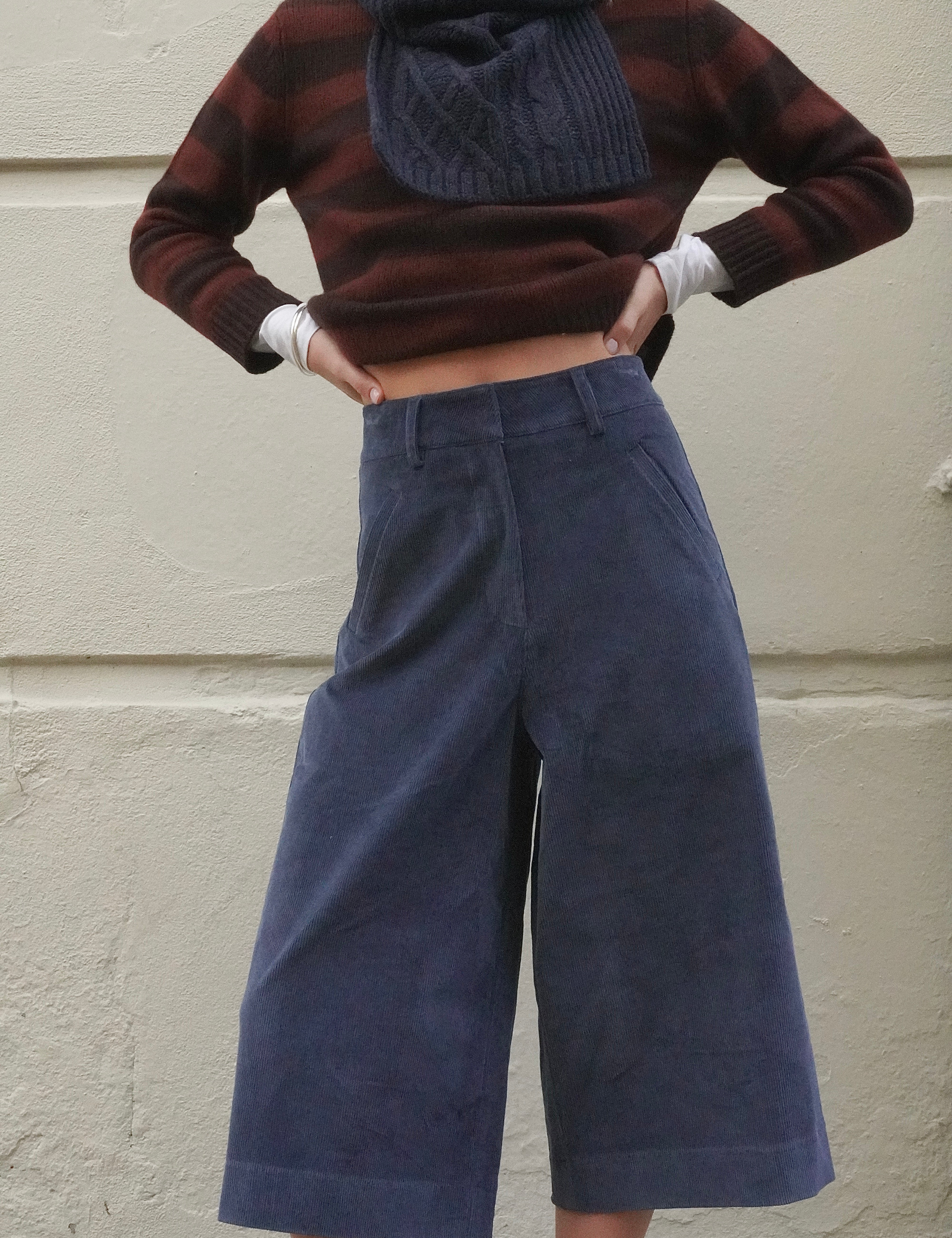 Woman wearing long blue corduroy shorts, with a brown striped cashmere jumper and navy scarf. 