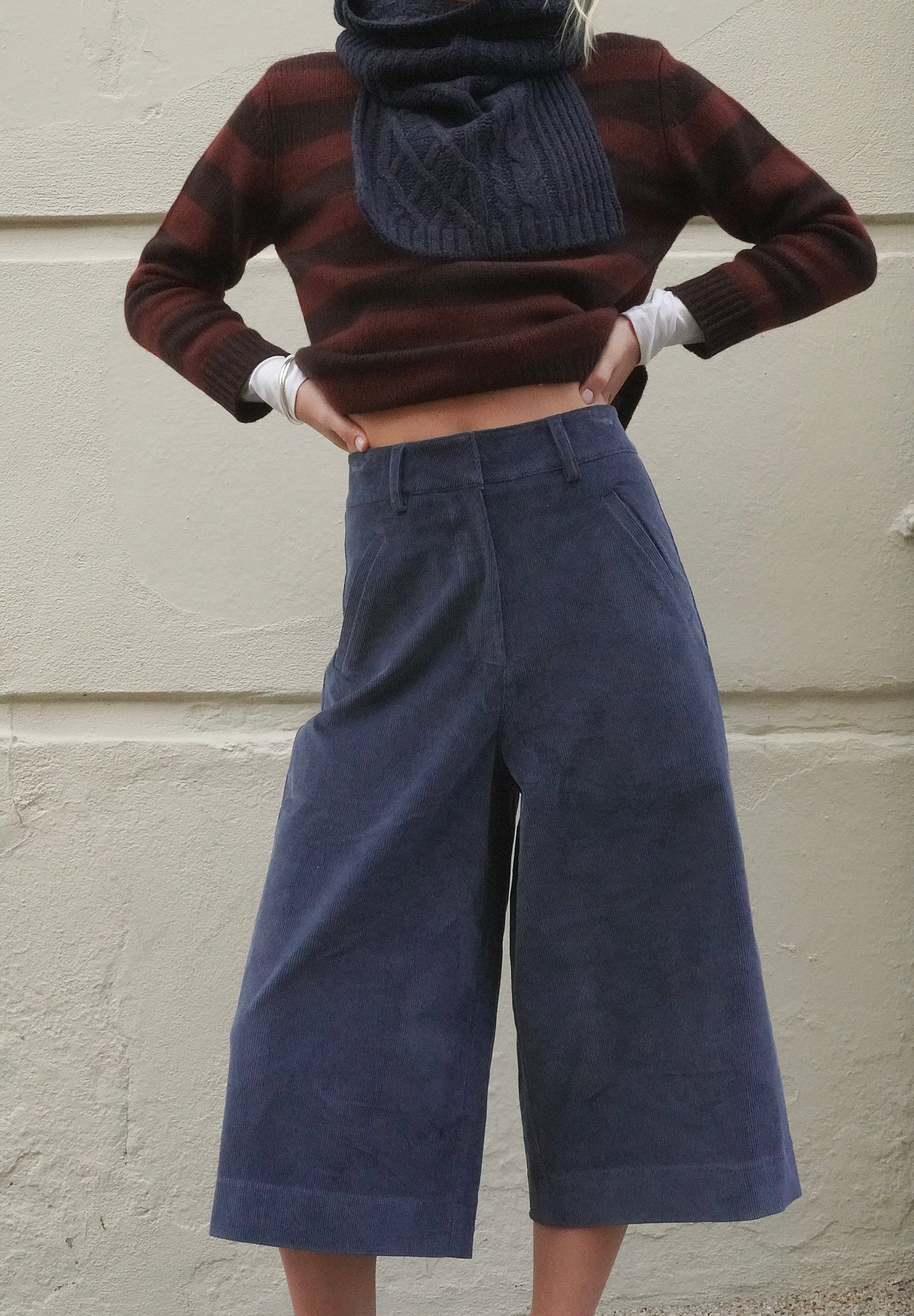 Woman wearing long blue corduroy shorts, with a brown striped cashmere jumper and navy scarf. 