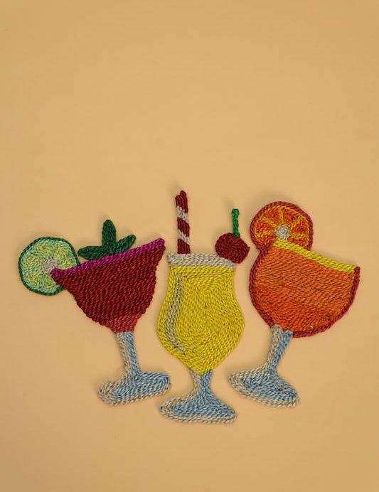 Three colorful embroidered cocktail patches on a solid beige background. The patches depict a red margarita with a lime wheel, a yellow drink with a striped straw and cherry, and an orange cocktail with an orange slice, all in blue stemmed glasses.