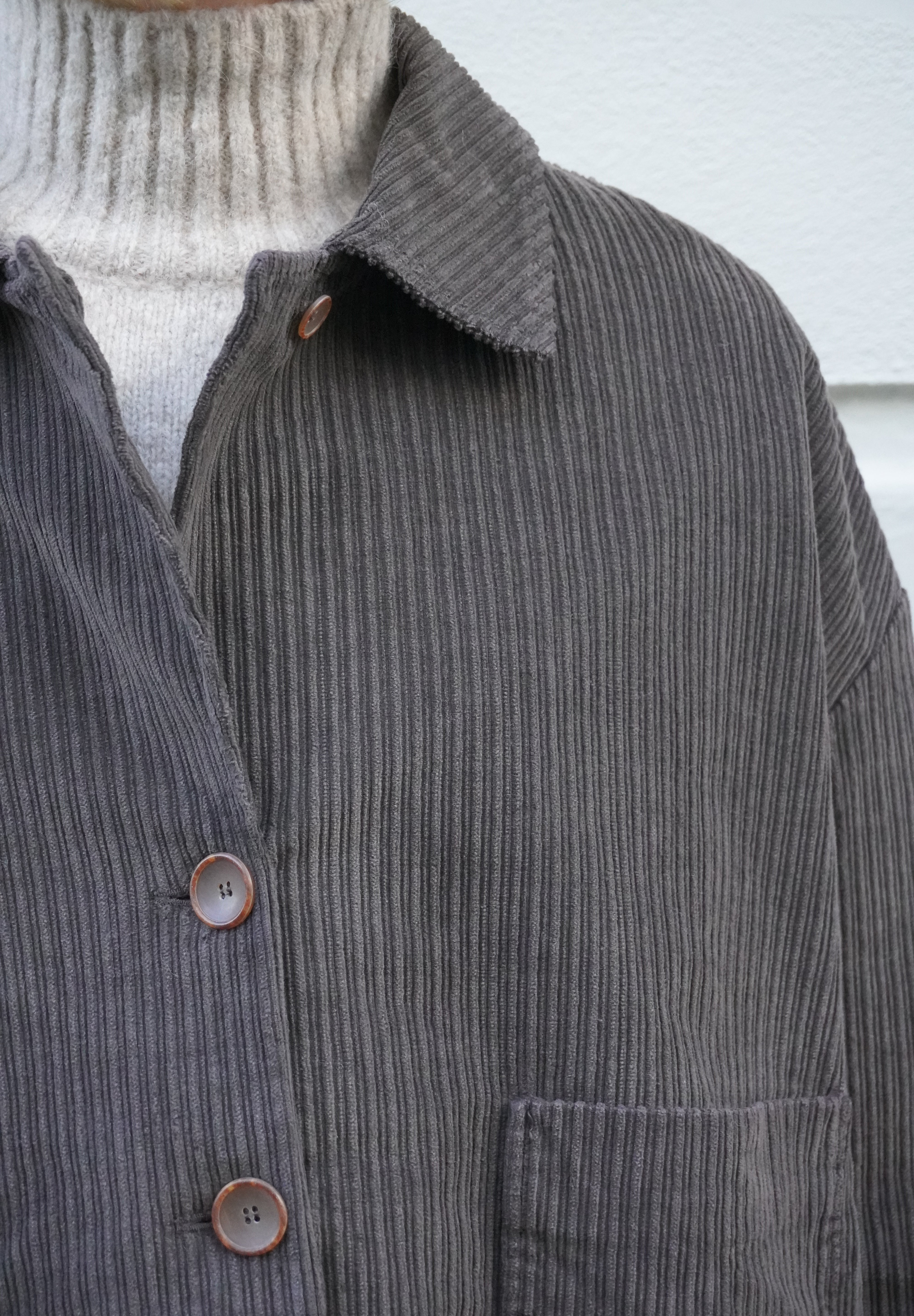 Close-up of a dark gray ribbed corduroy button-up shirt jacket worn over a light beige ribbed turtleneck sweater.