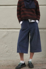 Woman wearing long blue corduroy shorts, with a brown striped cashmere jumper and navy scarf. 
