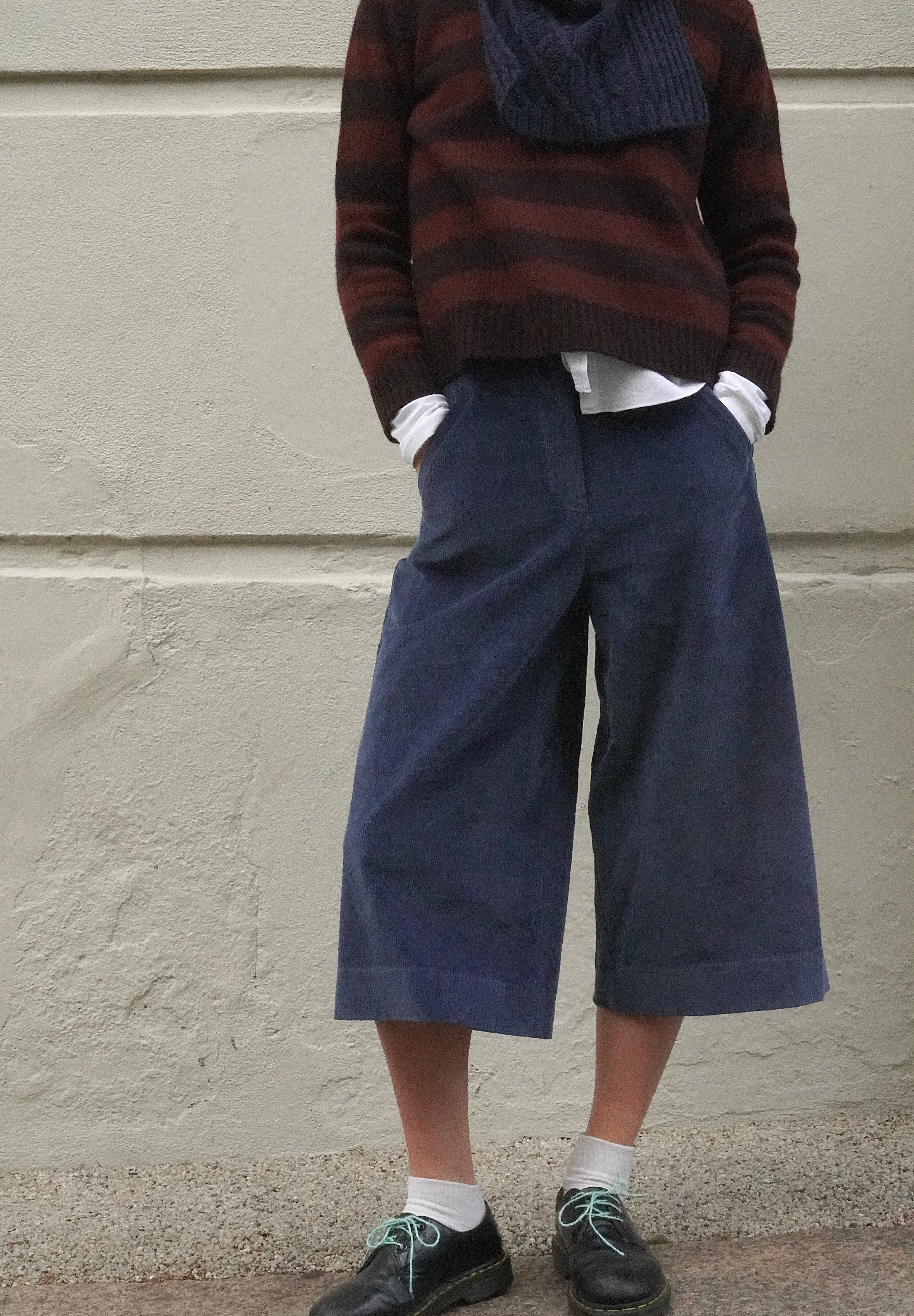 Woman wearing long blue corduroy shorts, with a brown striped cashmere jumper and navy scarf. 