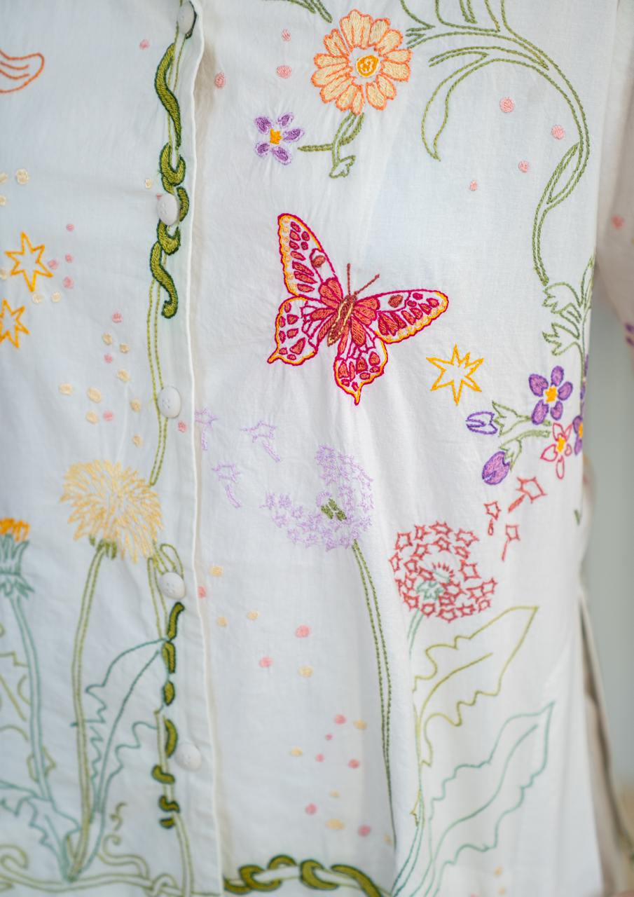 close up of embroidered pyjamas with long sleeves, shorts, with an unbleached white cotton background covered in embroidered multicoloured flower and butterfly motifs  