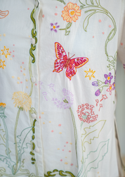 close up of embroidered pyjamas with long sleeves, shorts, with an unbleached white cotton background covered in embroidered multicoloured flower and butterfly motifs  