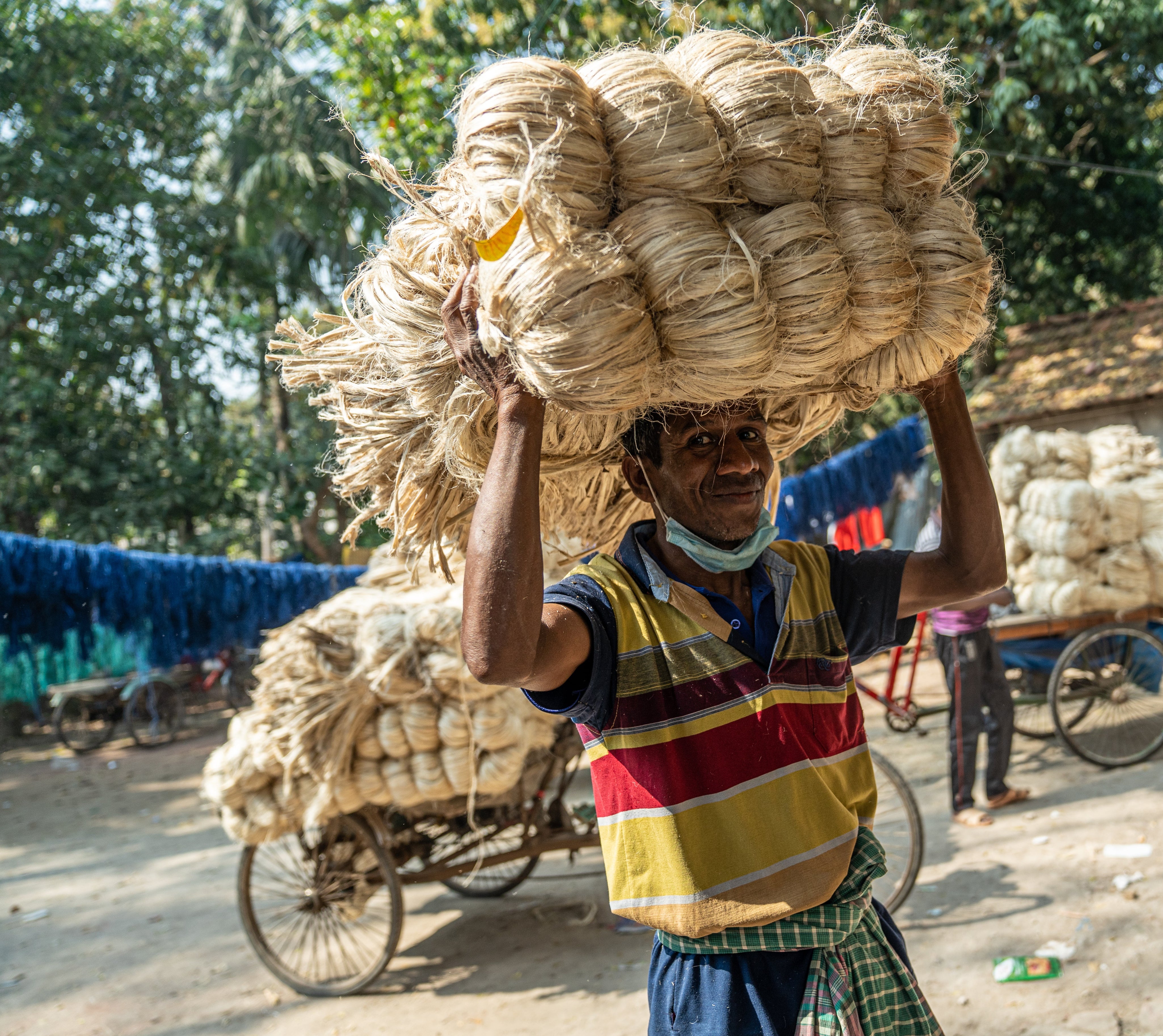 Man carrying a large bundle of raw jute on his head in an outdoor setting