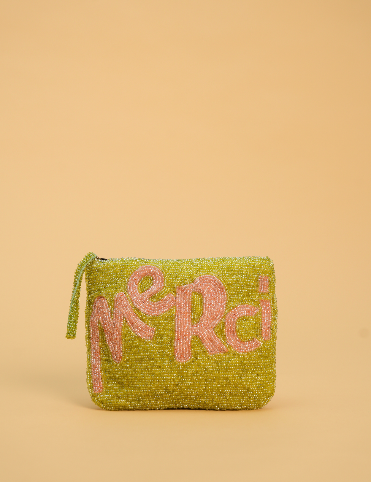 A small rectangular zip pouch covered in shimmering lime green beads, featuring the word 'merci' in pink beaded letters across the front, set against a solid beige background.
