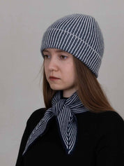 A woman wearing a navy and white striped knit beanie and a matching striped neck scarf, photographed against a plain light gray background.