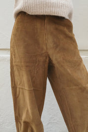 A close-up of a person wearing wide-leg brown corduroy trousers and a cream ribbed knit sweater, standing against a light textured wall.