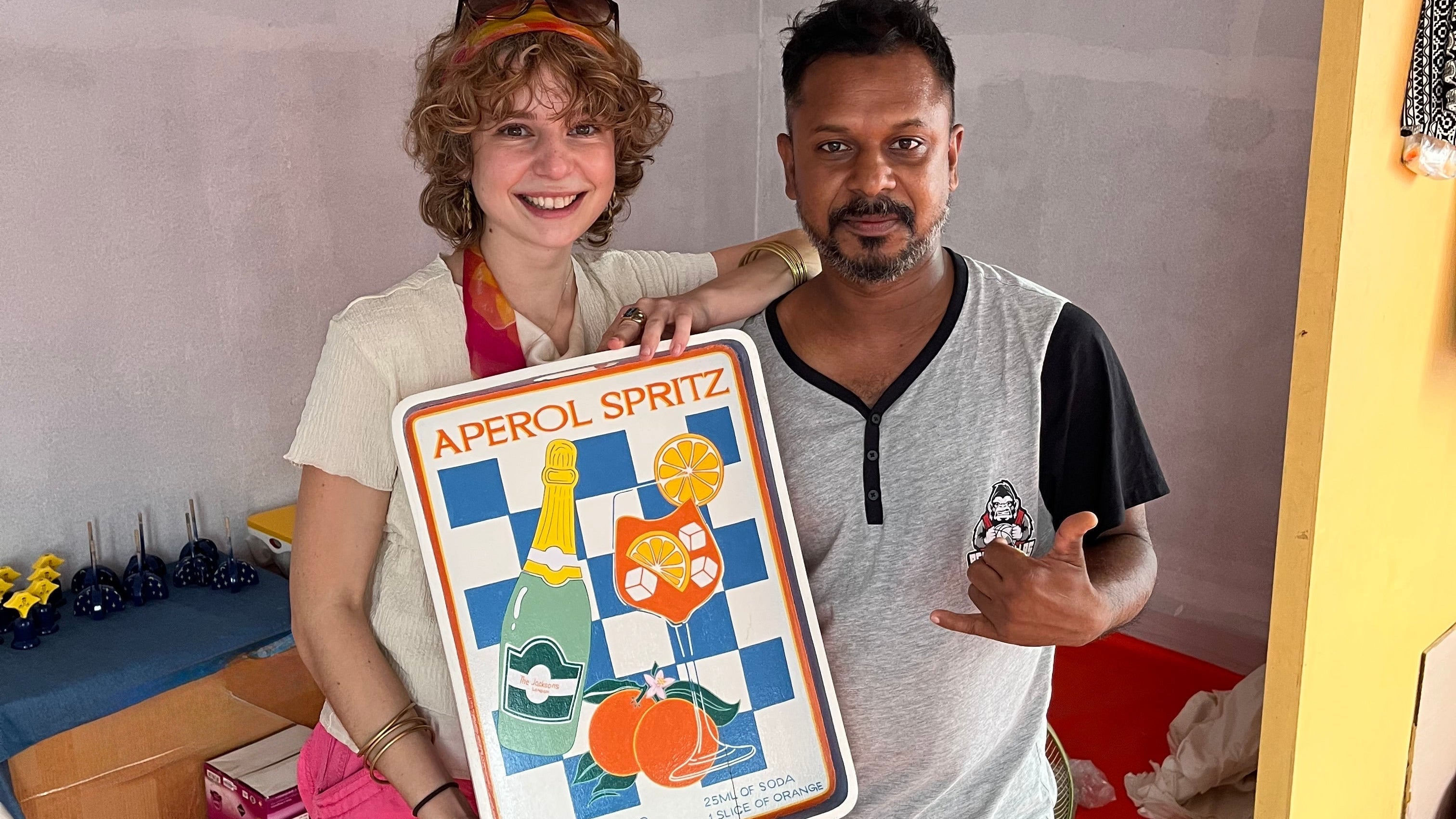 Two people holding a tray with 'Aperol Spritz' design.
