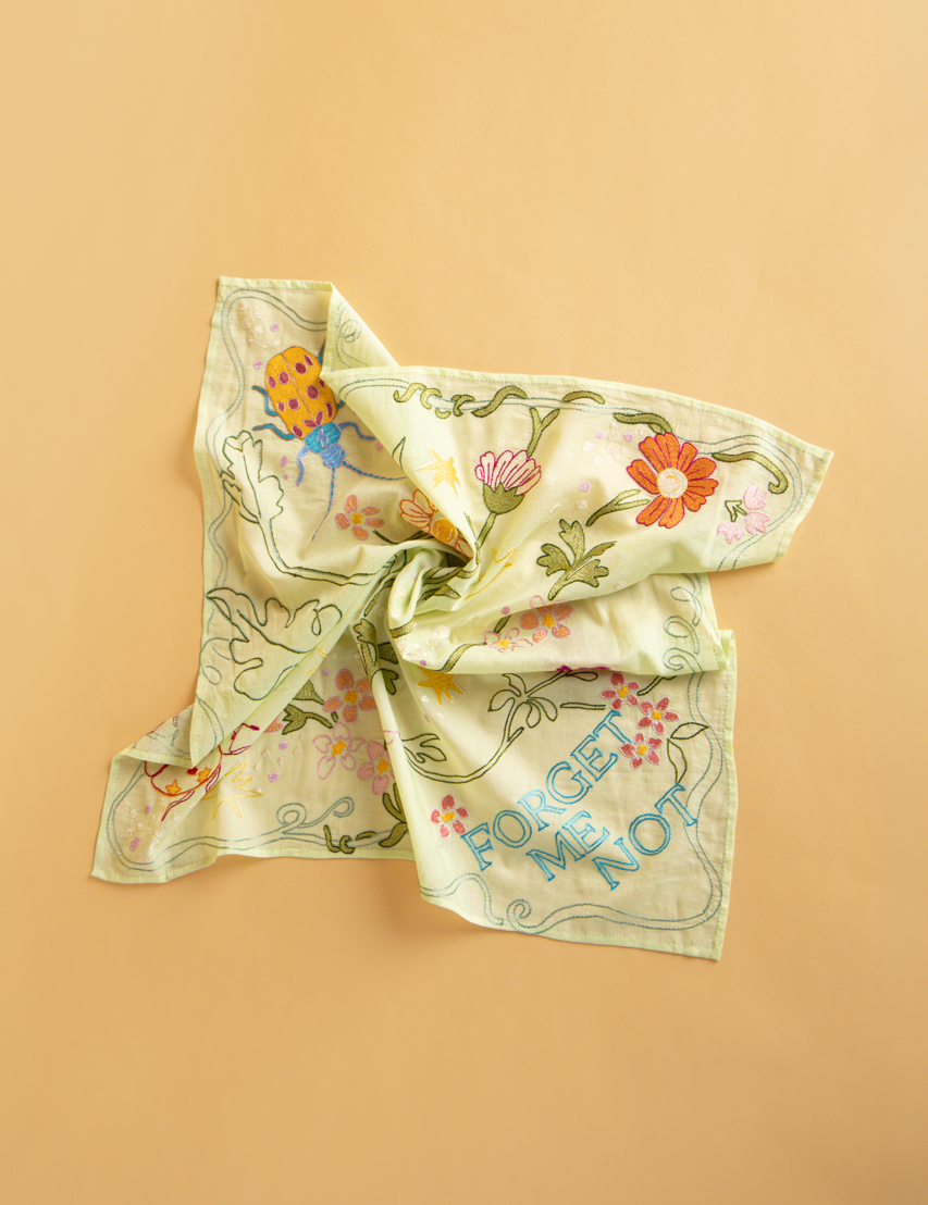 A square light green scarf with a floral pattern and the text 'FORGET ME NOT', displayed on a solid background.