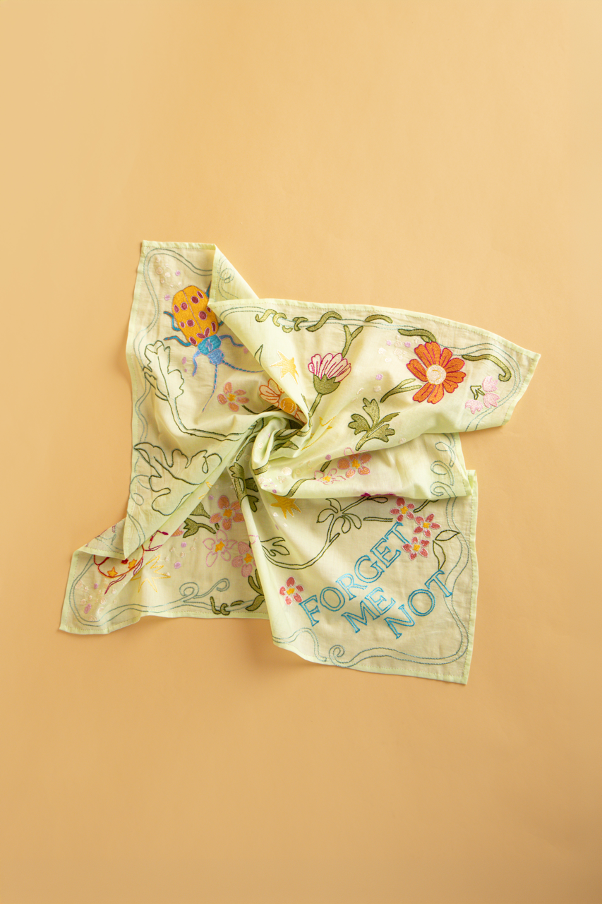 A square light green scarf with a floral pattern and the text 'FORGET ME NOT', displayed on a solid background.