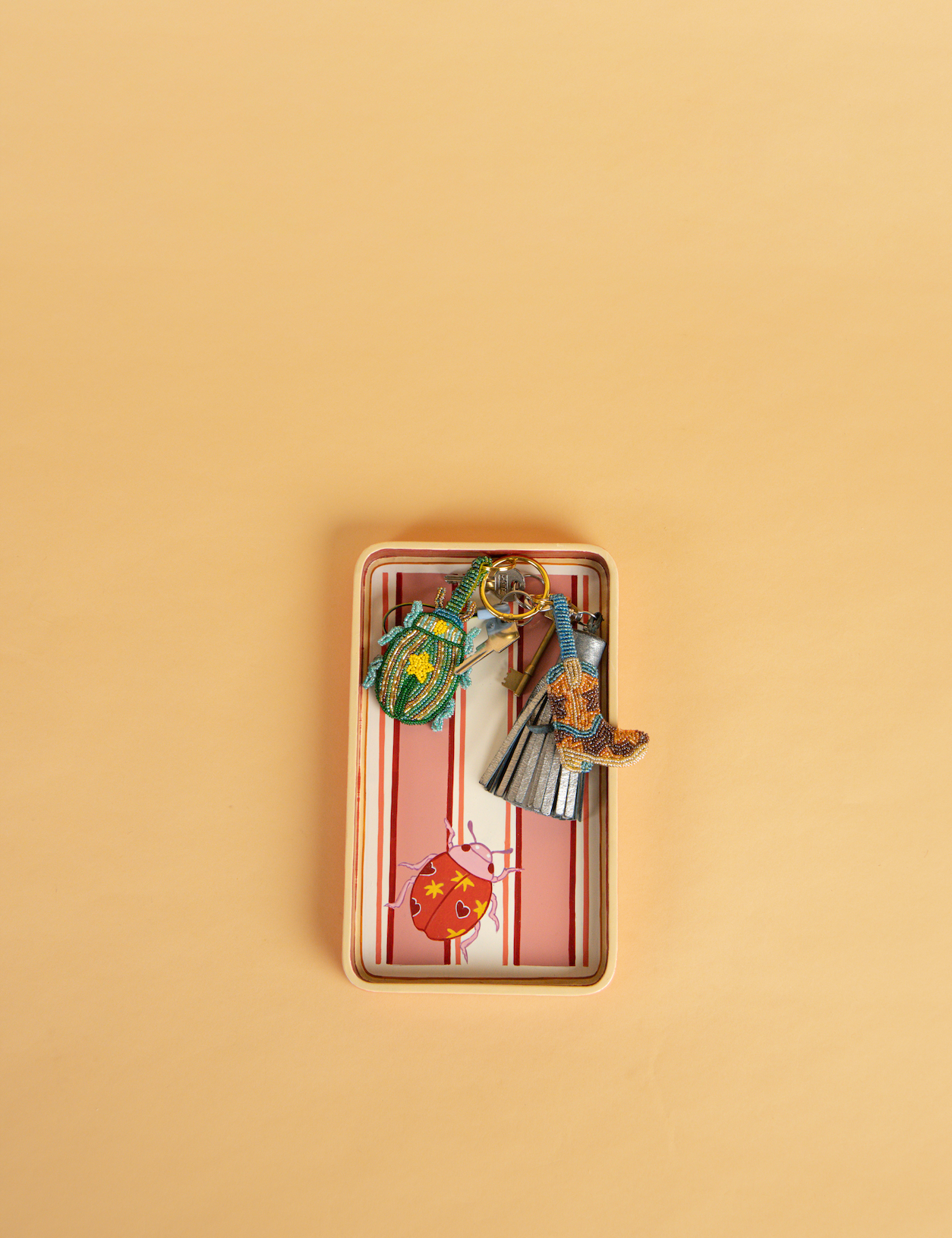 A small handpainted rectangular tray, with a pink and white striped pattern, containing several photographed from above on a solid beige background.