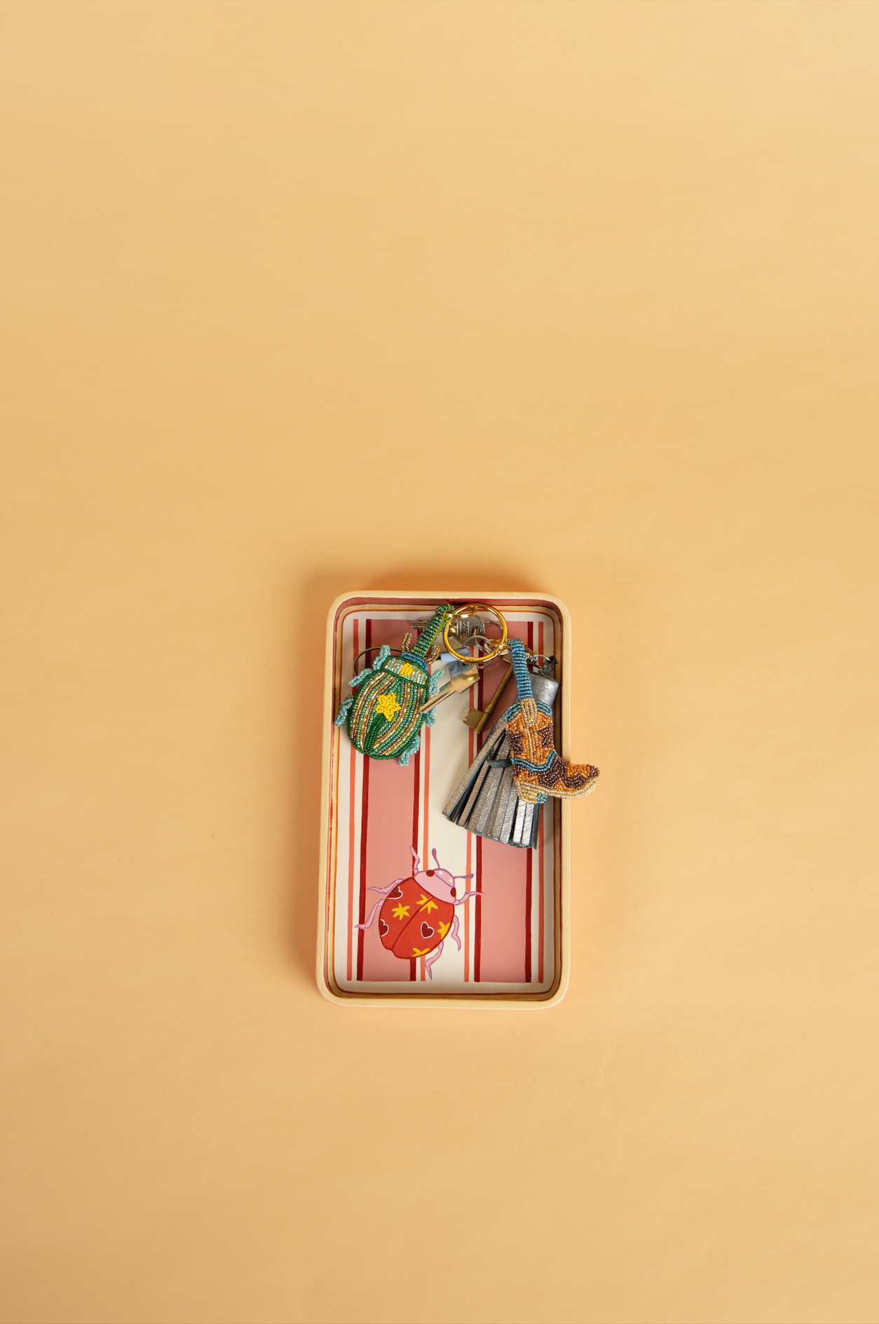 A small handpainted rectangular tray, with a pink and white striped pattern, containing several photographed from above on a solid beige background.