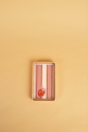 A rectangular wooden hand-painted tray with rounded corners, featuring vertical pink and white stripes and a small orange ladybird illustration near the bottom, set against a solid beige background.