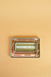 three handpainted wooden trays, with the words forget me not painted in sky blue, on a green and blue striped tray