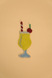 A tropical Piña Colada Coaster, with a red and white striped straw and cherry. The coaster is made from jute. 